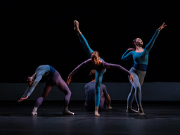 Against a dark background, a group of dancers performs on stage.