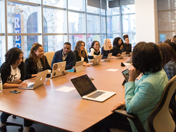 a diverse group of professionals with laptops seated around a large rectangular table