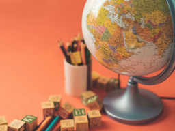 Picture of a world map globe on an orange desk, with pencil colors on top