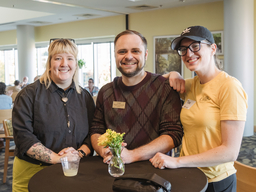 Three UMBC staff standing around a cocktail table wearing black and gold at the UMBC Homecoming faculty and staff social.