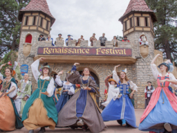 women in medieval costumes dancing in front of a Renaissance Festival sign