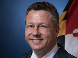 headshot of smiling man in front of the MD state flag