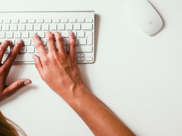 hands typing on a keyboard on a white desk
