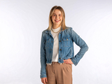 Madeline stands smiling wearing a blue denim jacket against a white background.