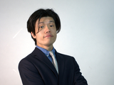 Jonathan stands in front of a white background wearing a blue suit.