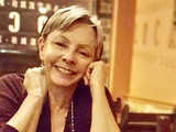 A white woman with short light hair smiling and sitting in a restaurant